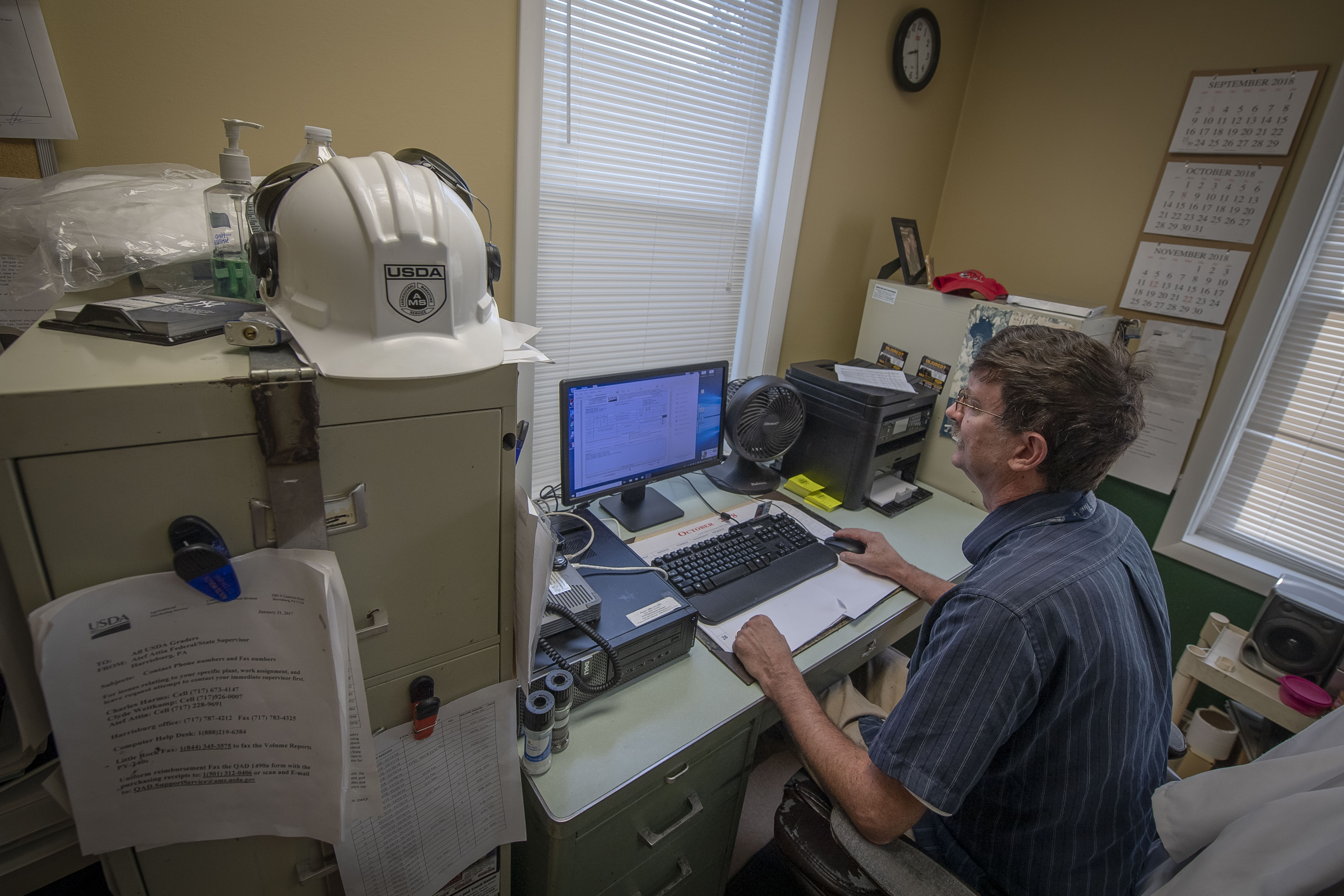 View of the back of a man sitting in front of his computer in his office.