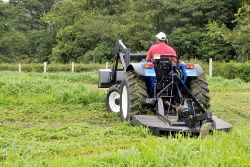 man driving a bush hog through a field